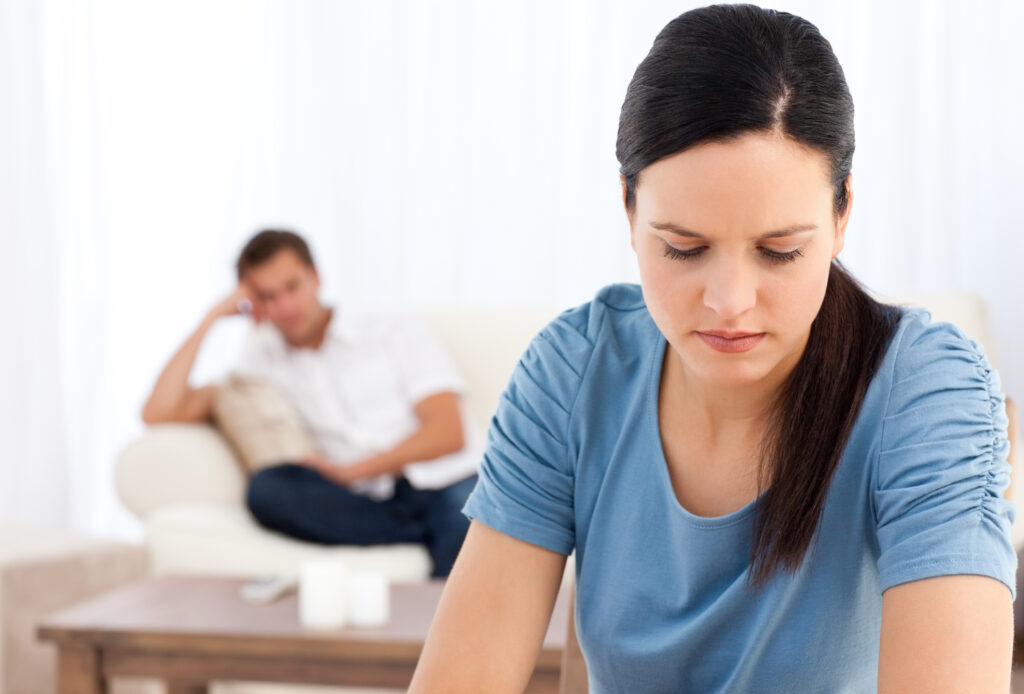 Woman thinking at a table while her boyfriend waiting in the background