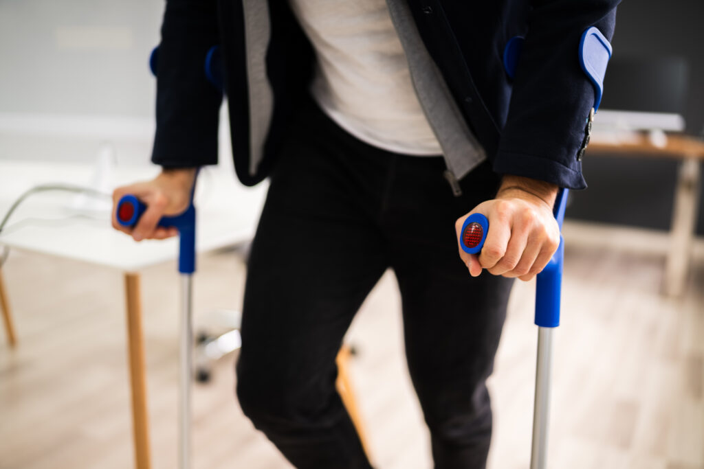 Disabled Man Standing With Crutches At Office Workplace